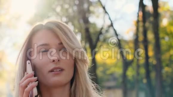 一幅美丽时髦的白人女性在智能手机上聊天享受在秋日公园散步的特写照片女孩视频的预览图