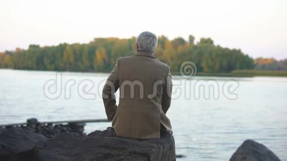 老年男性坐在石河畔思考生活欣赏自然风光视频的预览图