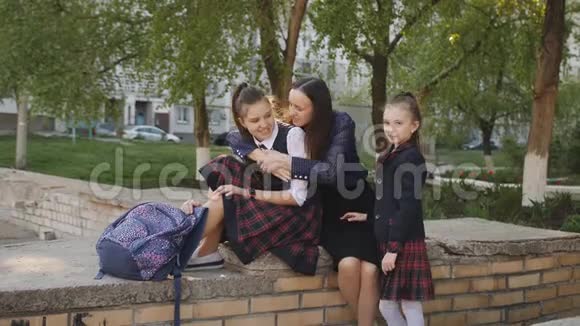 母亲带着两个穿校服的女儿背着背包坐在学校附近的街道上聊天视频的预览图