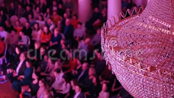 音乐厅的音乐会里面有一个大水晶吊灯人们坐在椅子上拍手视频的预览图