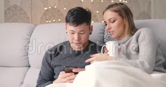 年轻夫妇坐在沙发上用智能手机视频的预览图