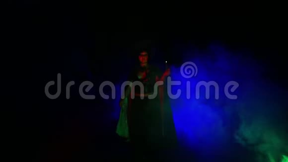 一个年轻的女人在一个女巫的形象在探照灯的灯光下从烟云中出现并拍打她的斗篷视频的预览图
