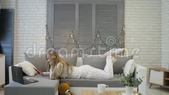 一个年轻的女孩躺在沙发上坐在沙发上从沙发上站起来心情愉快笑容灿烂视频的预览图