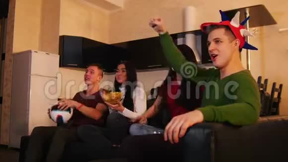 朋友们一起度过时光四个年轻人坐在沙发上看足球为球队加油视频的预览图