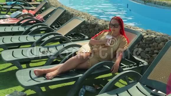 一位年轻女子在游泳池附近的一张躺椅上晒太阳视频的预览图