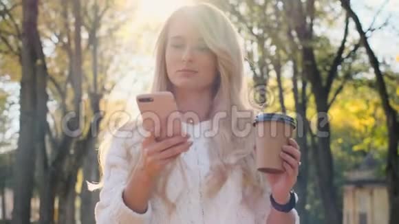 美丽的年轻时髦女孩穿着白色毛衣使用智能手机和喝咖啡在休息时散步视频的预览图