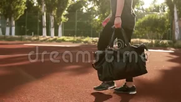 年轻漂亮的健身女子背着运动包在户外体育场散步没有脸太阳照耀着背景视频的预览图