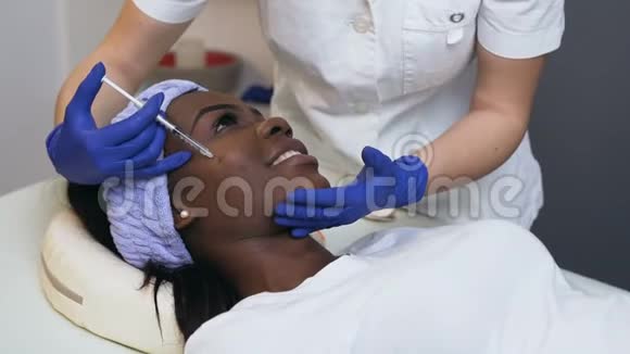 美容师为非洲年轻女性做美容注射的女性双手侧视视频的预览图