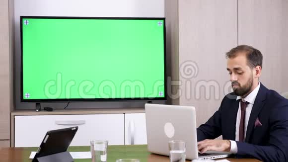 绿色屏幕电视旁边的笔记本电脑上的商人类型视频的预览图