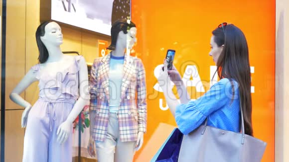 漂亮女孩用智能手机在商店橱窗里拍一张衣服并在社交媒体上分享视频的预览图