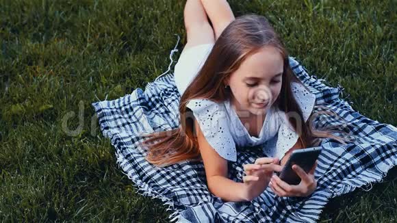 快乐女孩通过电话打短信躺在公园的草地上颜色分级视频的预览图