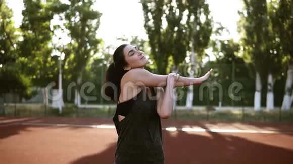 一个身穿运动服的活泼的黑发女孩伸展着她的双手肌肉热身户外体育场绿色视频的预览图