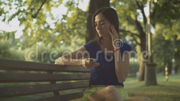 在公园长椅上欣赏音乐的美女视频的预览图