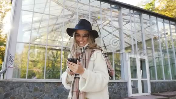 戴着帽子的年轻美女在城市公园里和朋友用智能手机聊天肖像拍摄视频的预览图