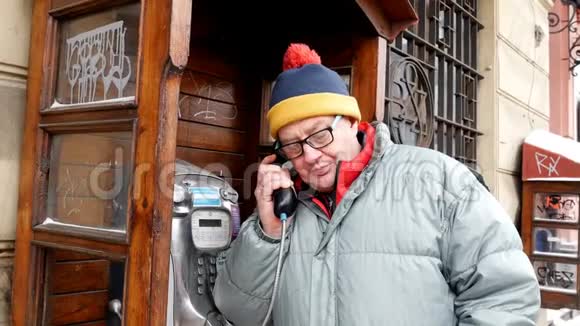 成年男子在街上的一个公共电话亭里用电话交谈视频的预览图