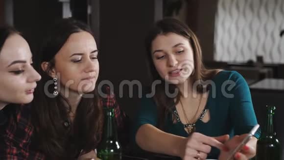 在餐厅里和年轻女孩一起在智能手机上看照片女孩吃披萨喝啤酒视频的预览图