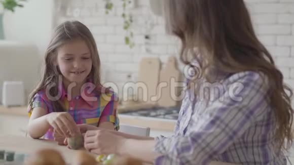 肖像母亲和可爱的女儿坐在复活节的桌子上小女孩画了一个带有细流苏的复活节彩蛋视频的预览图