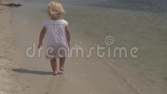 美丽的小女孩沿着海滨奔跑在海岸穿白色裙子的小女孩慢动作视频的预览图