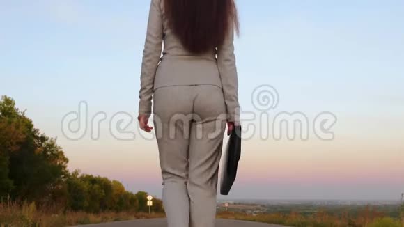 女商人手拿着黑色公文包手里拿着文件女人走在城外的柏油路上后景视频的预览图