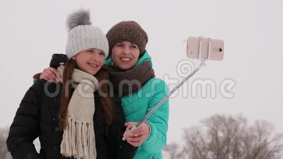 妈妈和女儿在智能手机上拍照在圣诞节早上的冬天公园一家人在白雪皑皑的树林里休息视频的预览图