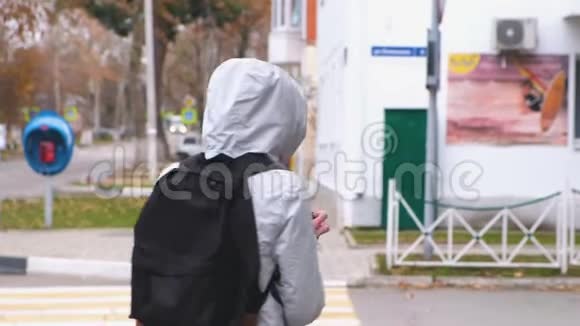 穿着白色夹克和背包的女人将在城市的一个人行横道上过马路视频的预览图
