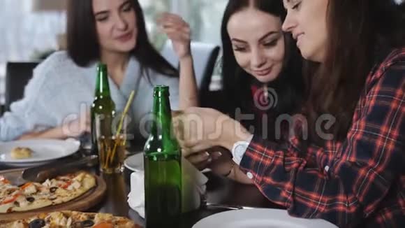 四个女孩正在餐厅放松喝啤酒吃披萨餐馆里的姑娘们看了电视上的录像视频的预览图