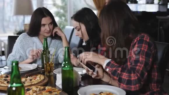 在餐厅里和年轻女孩一起在智能手机上看照片女孩吃披萨喝啤酒视频的预览图