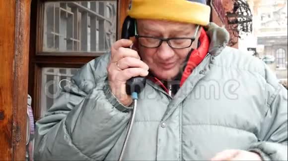 成年男子在街上的一个公共电话亭里用电话交谈视频的预览图