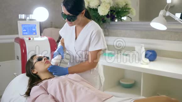 美容医生用激光设备在水疗中心的治疗室对病人面部进行脱毛视频的预览图