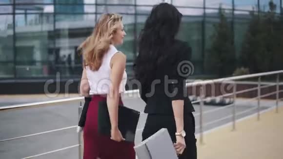 商业女性在商业中心的背景下使用文件夹两个穿着严格西装的女孩回来视频的预览图