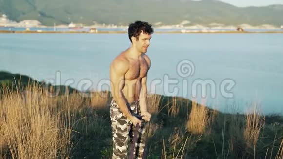 运动员在高山和大海的背景下用健身橡皮筋做运动视频的预览图