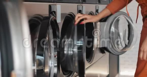 年轻的非洲裔美国妇女坐在洗衣机前给洗衣机装上脏衣服自助服务视频的预览图