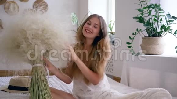 舒适的氛围无过敏症的年轻女性在睡衣的床上捧着一束羽毛草视频的预览图