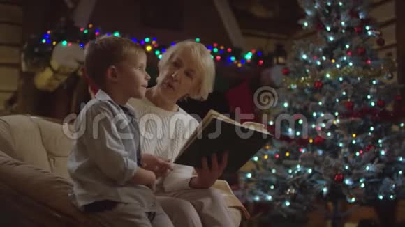孙子坐在她身边在圣诞夜和他说话祖父在为他读一本书视频的预览图
