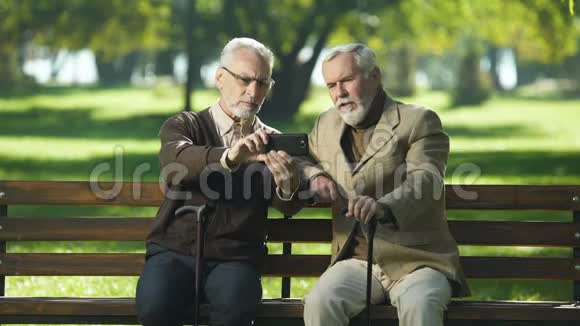 两名年长的男子坐在公园里用网络摄像机和朋友打电话视频的预览图