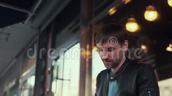 一个穿黑色皮夹克的男人在咖啡馆旁边低头看着视频的预览图