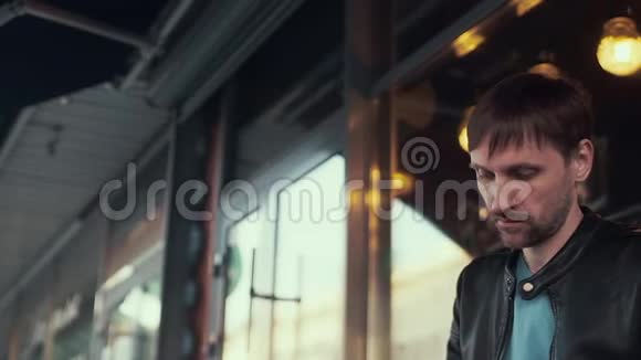 一个穿黑色皮夹克的男人在咖啡馆旁边低头看着视频的预览图