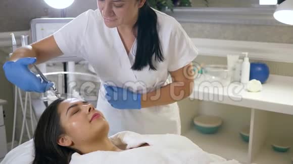 美容师在美容沙龙器械的帮助下用女性患者的皮肤面部进行复健视频的预览图