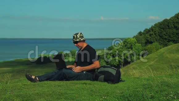 一个背着背包的人坐在山的边缘俯瞰湖面用笔记本电脑工作关闭视频的预览图