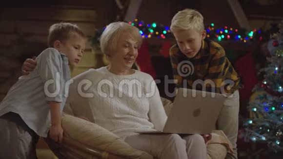 有两个小男孩的老太太在圣诞夜做笔记本电脑的视频翻译视频的预览图
