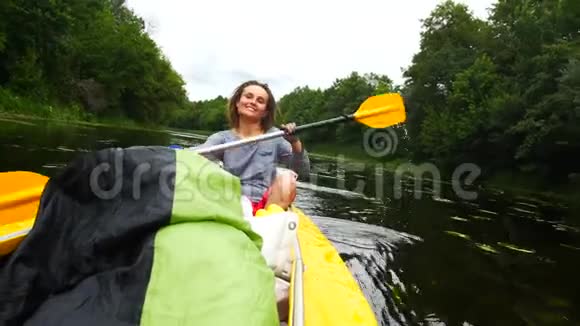 一个年轻的女孩在河上的皮划艇上用桨努力工作视频的预览图