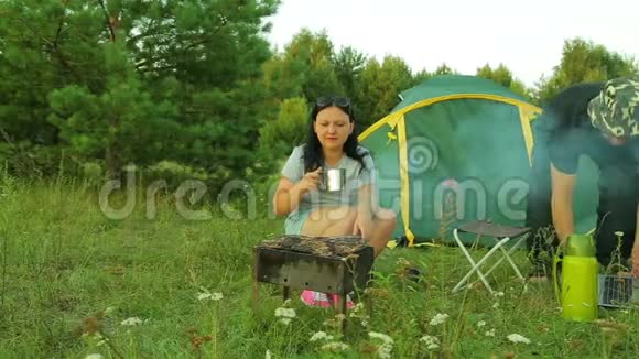 一个女人在帐篷附近的自然炸一个什什烤串和喝茶那个人坐在笔记本电脑旁边视频的预览图