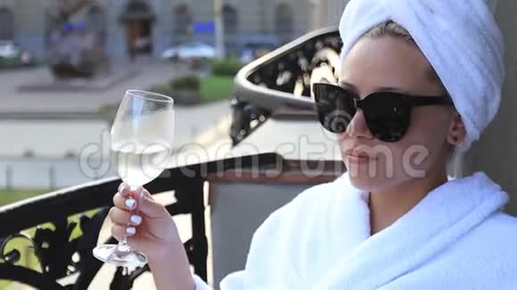 一个穿着白色浴袍头上戴着毛巾的女孩喝着一杯白葡萄酒视频的预览图