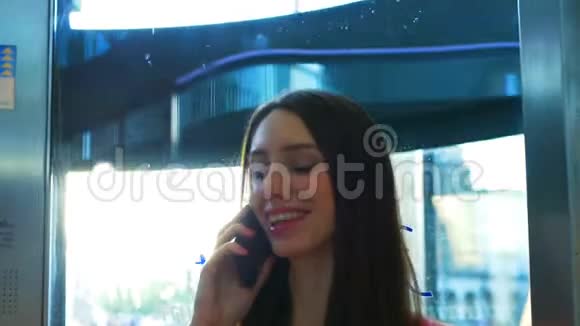 一个年轻的女孩正在智能手机上交谈在一台现代化的玻璃电梯里微笑着视频的预览图