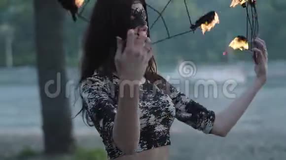 戴着面具的优雅女人的肖像在树前的河岸上表演着火焰熟练的射击技巧视频的预览图