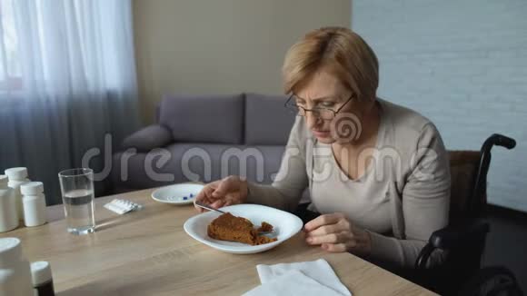 孤独的老奶奶坐在轮椅上慢慢地在桌旁吃着午饭视频的预览图