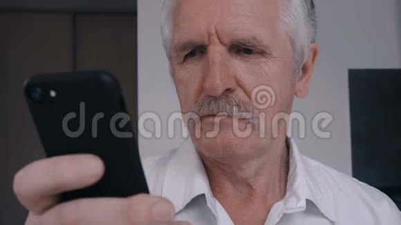 在厨房里用智能手机关闭有胡子的老人视频的预览图