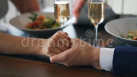 用香槟酒杯和餐盘将女性的手举在桌子上的男性手的特写镜头浪漫浪漫视频的预览图