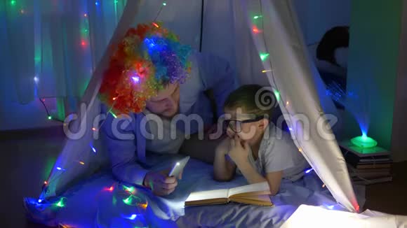 家庭娱乐快乐的孩子与爸爸进入有趣的假发阅读书在手电筒躺在神奇的帐篷与神奇的帐篷视频的预览图