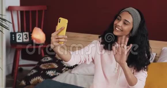快乐的非裔美国女孩坐在homec的床上和她的朋友们一起在视频中打她的黄色电话视频的预览图